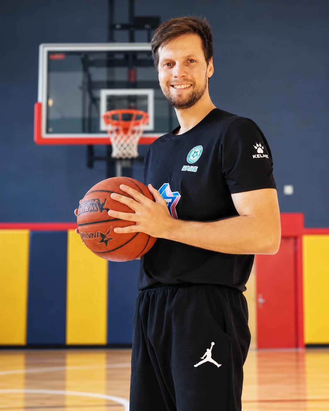 Coach Stefan Stankovic smiling with a basketball in a gym